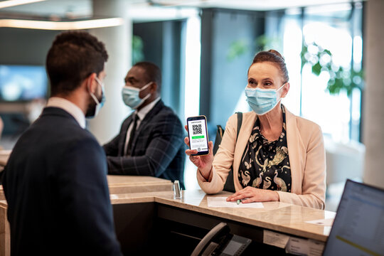 Middle aged businesswoman showing the certificate of her vaccination on a smartphone at the reception of a hotel