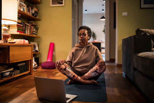 Senior African American woman doing yoga with the help of her laptop at home