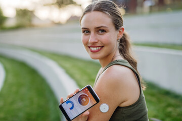 Woman with diabetes checking blood glucose level outdoors using continuous glucose monitor.