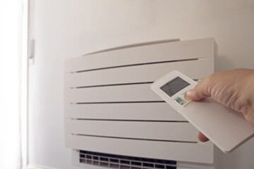 Human hand uses remote control, presses buttons, sets selects temperature of air cooling in home...