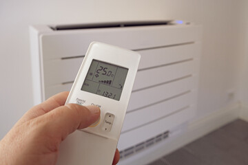 Human hand uses remote control, presses buttons, sets selects temperature of air cooling in home...