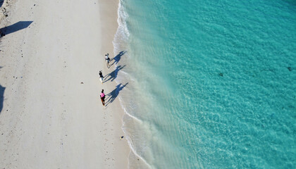 Aerial drone view of three persons riding on a horses on a beautiful sandy beach with white sand very close to the Indian ocean coastline. Aerial drone shot, Nungwi beach, Zanzibar