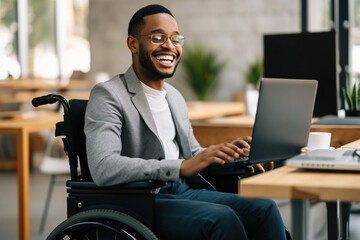 Smiling African American businessman with disability using laptop in wheelchair at workplace