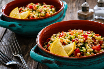 Tabbouleh salad -  bulgur groats, tomatoes, cucumber, parsley, lemon, onion and fresh mint leaves on wooden background
