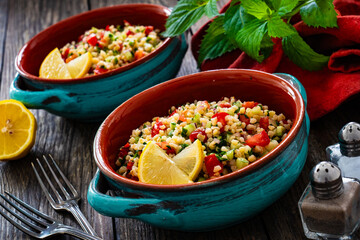 Tabbouleh salad -  bulgur groats, tomatoes, cucumber, parsley, lemon, onion and fresh mint leaves on wooden background

