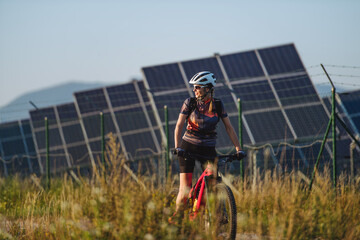 Beautiful cyclist riding in front of solar panels at a solar farm.