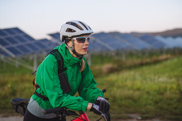 Fototapeta na wymiar Portrait of a beautiful cyclist standing in front of solar panels at a solar farm.