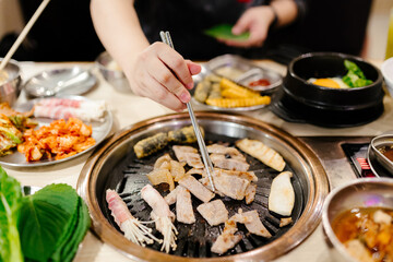 A woman's hand uses silver chopsticks to grill Korean-style pork.