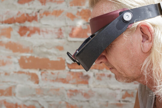 A man with a headlamp bowed his head over his work, against the backdrop of a brick wall. A device for working with small parts, soldering, and jewelry