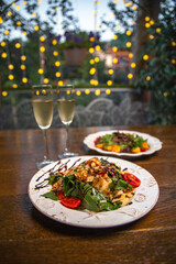 two plates of warm salad and glasses of wine on the wooden table of the summer cafe