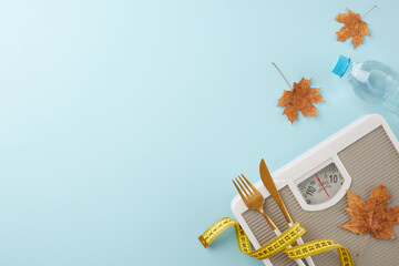 Autumnal weight loss and toning. Top view photo of weight scale, cutlery, tape measure, water bottle, dry maple leaves on pastel blue background with promo zone