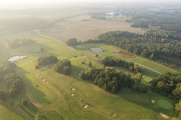 Aerial view of a big golf course during sunset, warm sunlight, green mowed grass