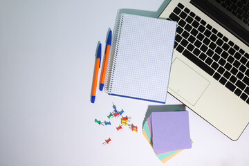 on a white background white laptop, white computer mouse, notepad, pens
