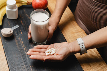 Athletic woman in sportswear holding glass of protein drink cocktail and white capsules of amino...