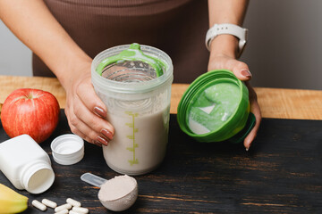 Athletic woman in sportswear holding shaker with protein drink cocktail on a table with white...