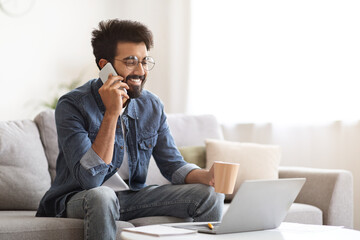 Young Indian Man Talking On Cellphone While Sitting On Couch At Home