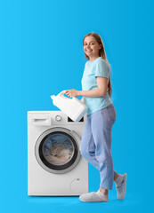 Pretty young woman adding detergent into washing machine on blue background