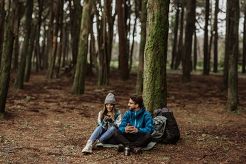 Fototapeta premium Smiling young caucasian guy, lady in jackets take break, relax, drink coffee from thermos, enjoy lifestyle