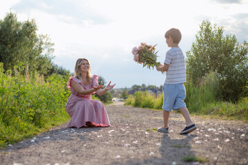 Fototapeta premium Boy congratulates his mother, gives her bouquet of peonies on summer day on country road. Single.