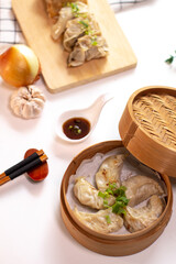 Close up of Gyoza dumplings cooked in bamboo steamer on white background served with napkin, chopstick, sauce and ingredient on the side. Top view