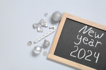 Blackboard with text NEW YEAR 2024 and Christmas decorations on grey background