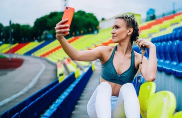 Fototapeten Braided sporty young woman capturing selfie by mobile in grandstand © BullRun