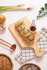 Hot gyoza dumplings on a wooden board, served with napkin, chopstick, sauce and ingredient on the side. white background