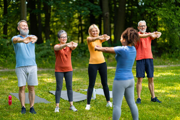Group of senior people having fitness class outdoors, training with female instructor
