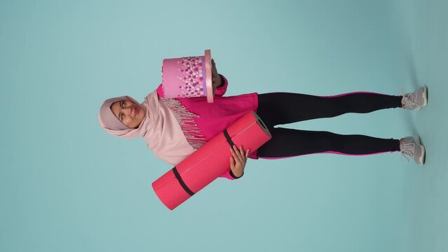 Full-sized isolated video capturing a young woman in a sportswear and a hijab, sheila choosing between a cake and an exercising mat, throwing a mat away.