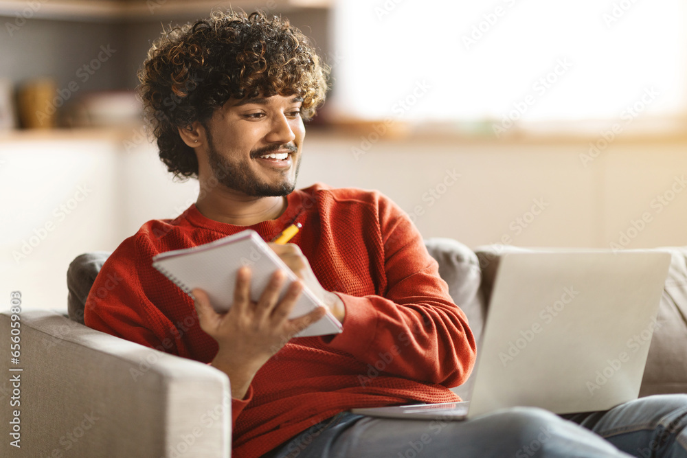 Sticker distant learning. smiling indian guy using laptop and taking notes to notepad