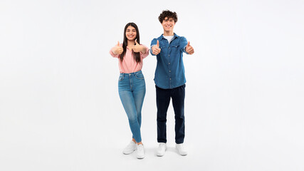 Full length of girlfriend and boyfriend gesturing thumbs up, studio