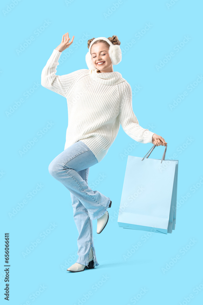 Sticker happy young woman in warm sweater and fluffy headphones with shopping bags on blue background