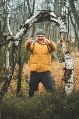 Portrait of young laughing friendly man, that pose with his hands and stands under bending tree, during cold cloudy autumn day, Decin, Czech republic