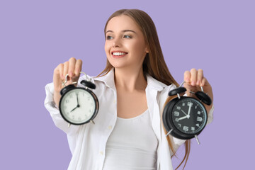 Pretty young woman with alarm clocks on lilac background
