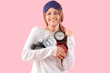 Happy young woman with alarm clocks on pink background