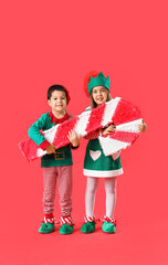Cute little children dressed as elves with candy cane pinata on red background