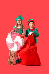 Cute little children dressed as elves with pinata and bag of gifts on red background