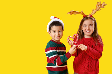 Cute little children with candy canes on yellow background