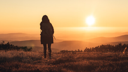 Woman walking with hands in pocket on a mountains peak when sun is going down, beautiful sunset in Krkonose, Czech republic