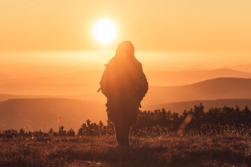 Woman walking with hands in pocket on a mountains peak when sun is going down, beautiful sunset in Krkonose, Czech republic
