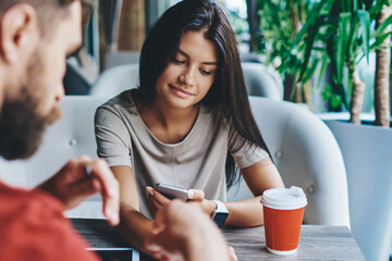 young woman share multimedia files from smartphone via bluetooth talking with hipster guy in cafe