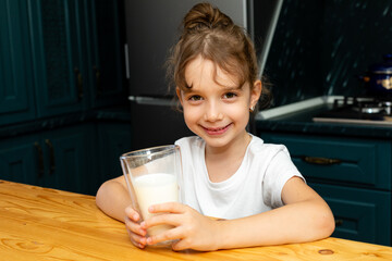 Cute little girl with glass of milk at table in a wooden kitchen, Happy child girl drinks milk. Milk Day. healthy breakfast