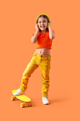 Cute little girl in headphones with skateboard on orange background