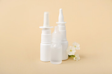 Bottles of nasal drops with flowers on beige background