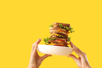 Female hands holding plate with tasty sandwich on yellow background, closeup - Powered by Adobe