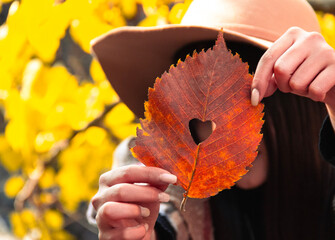 Autumn is beautiful. the girl is holding a leaf in her hand, and there is a heart in the leaf
