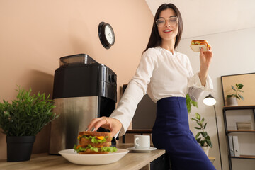 Young businesswoman with tasty sandwiches in office