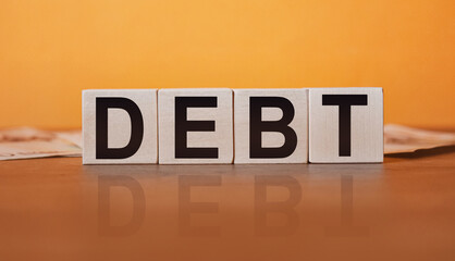 DEBT - an inscription on wooden cubes on an orange background along with banknotes. Finance and wear concept.