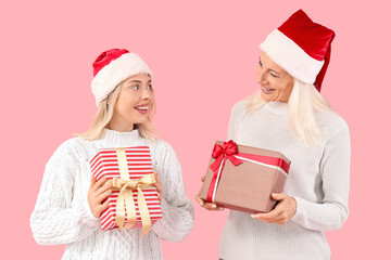 Happy daughter and her mother in Santa hats with gift boxes on pink background
