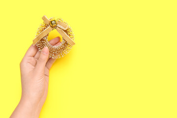 Female hand with beautiful Christmas decoration on yellow background, closeup